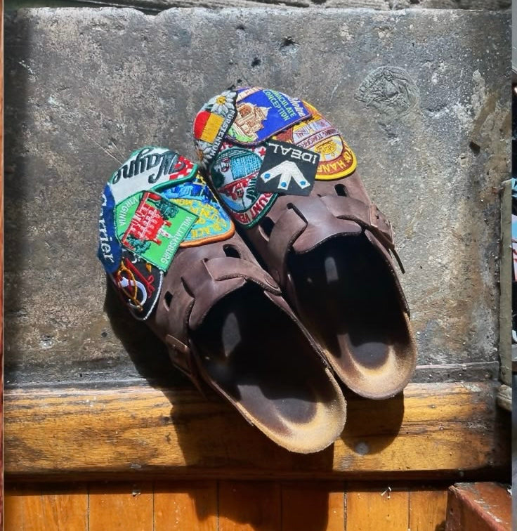 Pair of brown sandals with colorful patches on a stone surface.