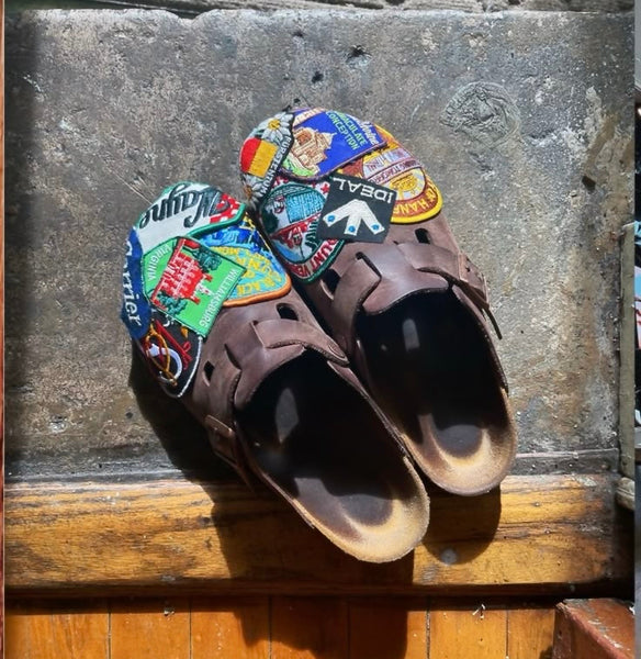 Pair of brown sandals with colorful patches on a stone surface.